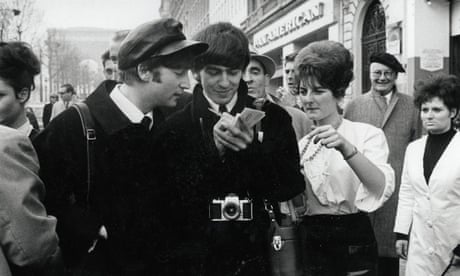 John Lennon (L) and George Harrison sign an autograph during a walk along the Champs Elysees, Paris, 1964.