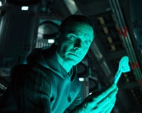 Michael Fassbender, lit in teal, examines a small robotic device in a scene from Alien: Covenant