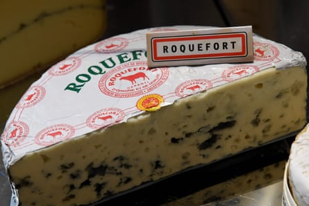 A half-moon of roquefort, showing its blue veins in a creamy centre. Its packaging bears a red stamp with the AOP designation.