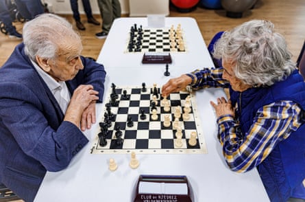 An elderly man and woman play chess.