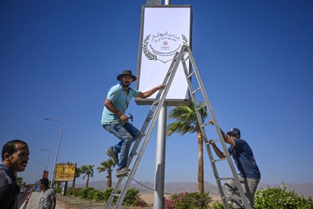 Municipal workers use a stepladder to attach a sign to a lamppost