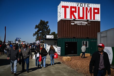 People walk past a large shipping container painted "VOTE TRUMP" at an agricultural expo
