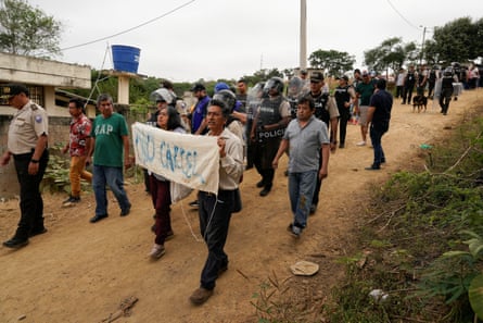 Latinos segurando uma faixa caminham por uma estrada de terra seguidos pela polícia