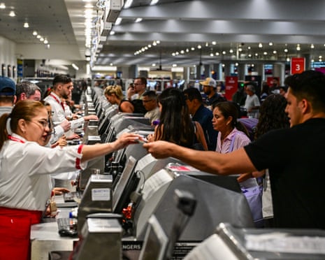 A row of airline check-in staff photographed from one end as they deal with passengers