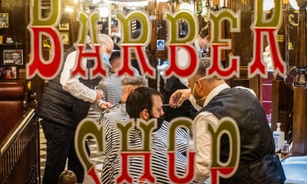 barber shop sign on a window and barbers cutting men's hair behind it