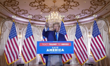 Trump speaking from a lectern with six American flags behind him and a chandelier overhead