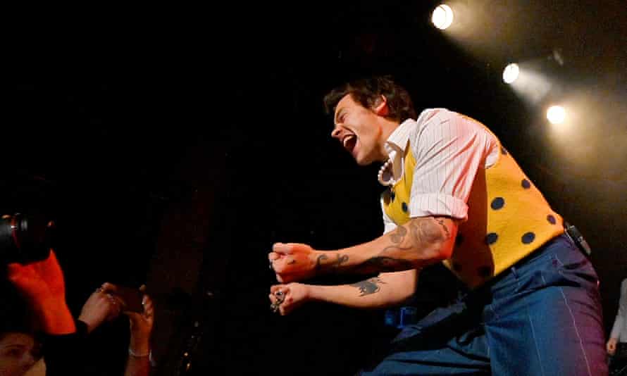 Harry Styles on stage in New York City in February wearing a striped shirt and tank top.