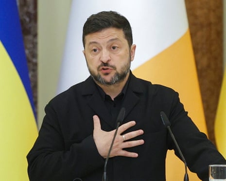 Volodymyr Zelenskyy gestures as he speaks into microphones