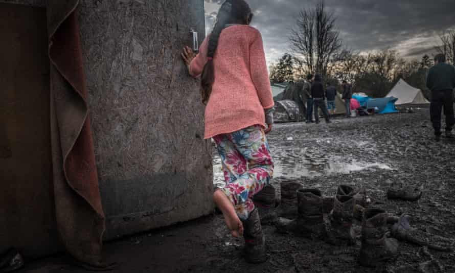 A girl tries on mud-caked boots in the camp.