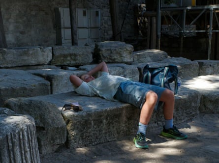 A boy lays back on a stone block in the shade