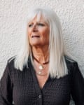 A mid portrait of a woman with white fringed straight hair beyond her shoulders wearing a brown cardigan looking to her right