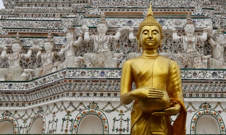 A Buddha statue stands in front of the ancient pagoda at the Wat Arun, or Temple of Dawn, in Bangkok, Thailand