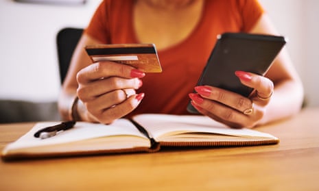 Woman looking at a debit card in one hand with her smartphone in the other