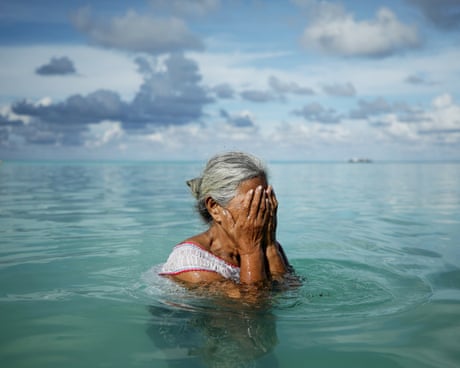 An older woman with her hands over her face in an aqua sea