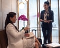 A woman sits on a leather chair with a book and coffee while an aiport lounge attendant stands next to her