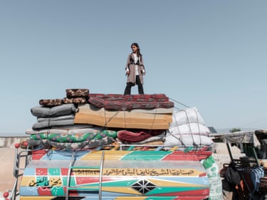 A girl stands on top of a pile of mattresses on a tractor