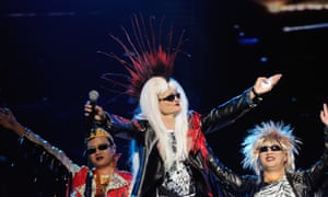 Jack Ma, in a leather jacket, sunglasses and a wig giving him a Mohican haircut combined with long blonde hair, gestures to the crowd in a rock-star pose