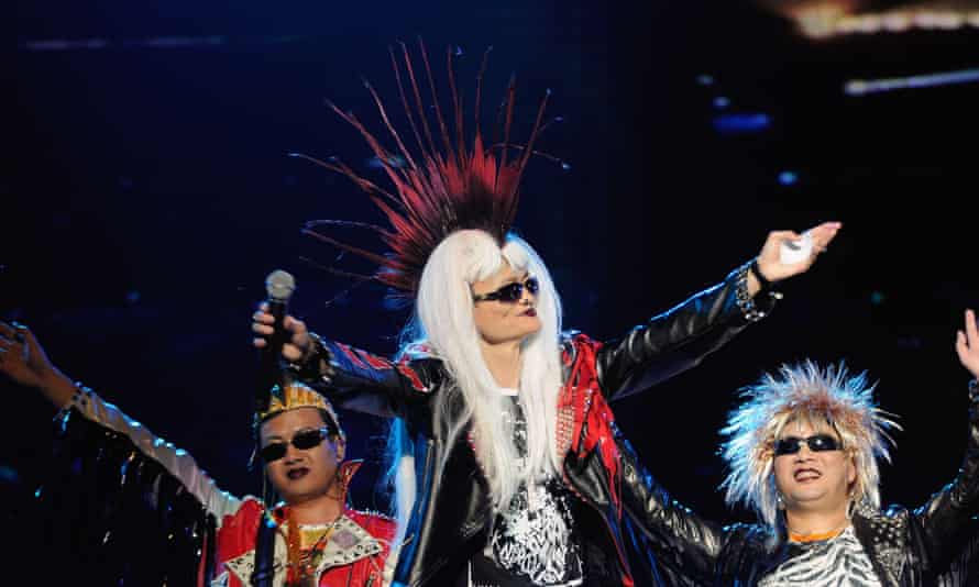Jack Ma, in a leather jacket, sunglasses  and a wig giving him a Mohican haircut combined with long blonde hair, gestures to the crowd in a rock-star pose