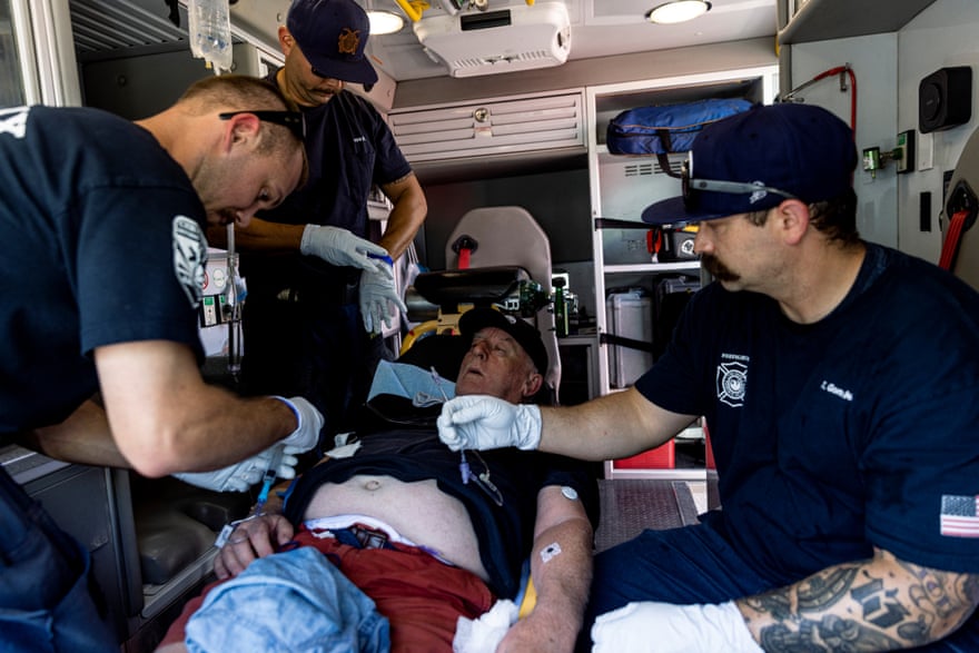 Paramedics prepare an IV for a man inside an ambulance