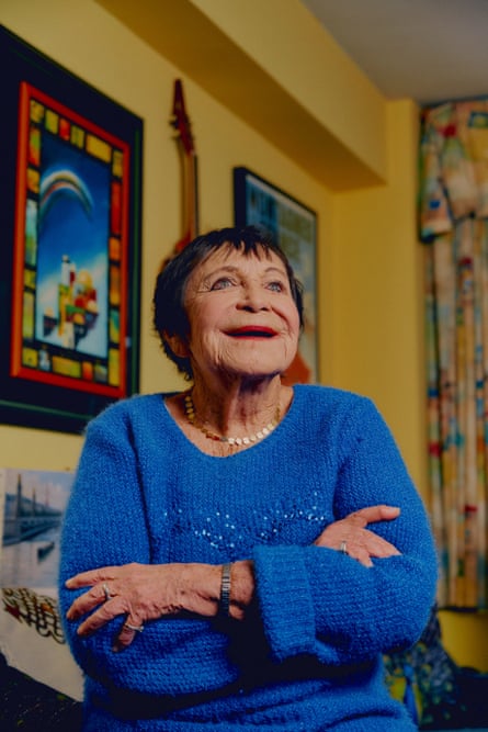 D’yan Forest photographed smiling, wearing a blue sweater with paintings in the background