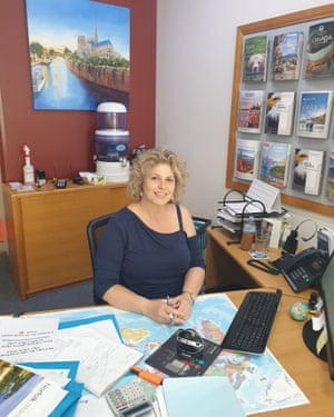 blonde woman sitting at a desk with travel brochures in background