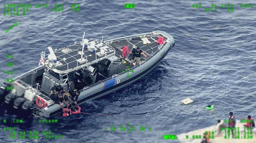 A US coast guard boat rescues people in brightly colored life jackets from the ocean.