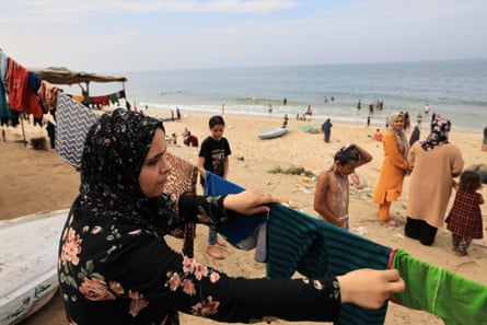 A Palestinian woman hangs out her laundry with other women and children on the beach in the background.