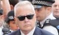 Huw Edwards wearing sunglasses and surrounded by police officers