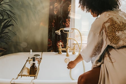 A woman testing the temperature of her bath water as she fills the tub. 