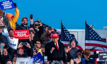 Donald Trump surrounded by supporters with US flags and 'Make America Great Again' placards.