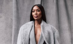Naomi Campbell poses in a grey suit and coat against a grey backdrop