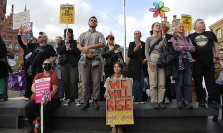 Jade Anderson holding a “We will rise – enough is enough” sign at a rally with other people standing on a low wall