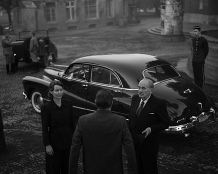 A black and white image of people stood next to an old car