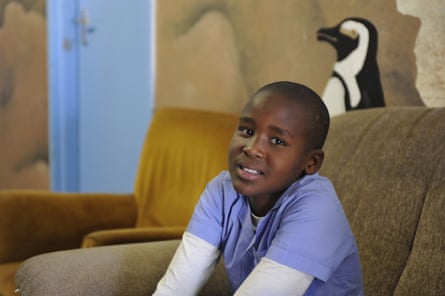 An African boy on an armchair, looking a bit worried, with a picture of a penguin on the wall behind him