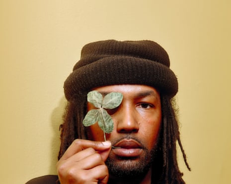 A man in a beanie holds a four-leaf clover over his right eye