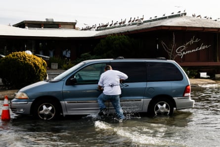 man walks through floodwater to open minivan door