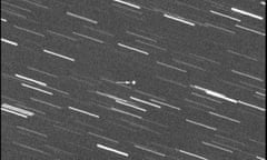 A grayscale photo of a distant asteroid appearing as a dot against a background of stars.