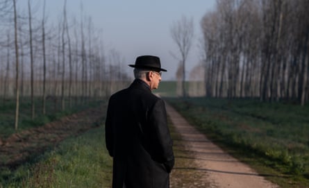 A man standing on grass with a long line of bare trees beside him