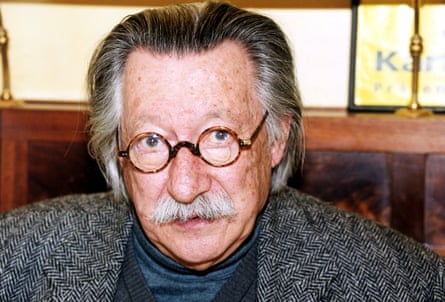 An elderly man with round glasses and swept-back grey hair.