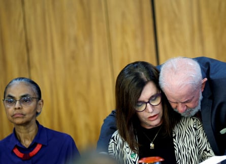 President Luiz Inácio Lula da Silva leans over the shoulder of Magda Chambriard to sign a document, while Marina Silva sits on their left