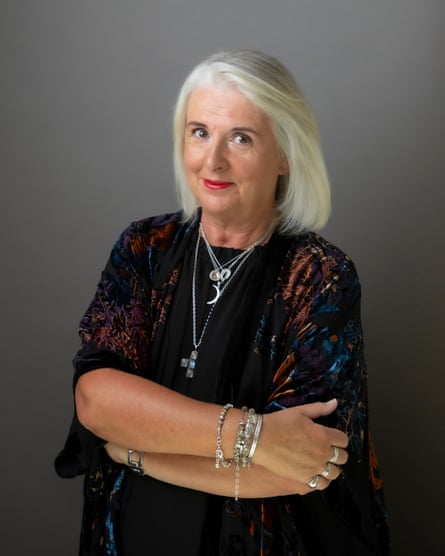 Barbara Scully poses for a photo. She is wearing a black top and a cardigan, plus several silver necklaces. She is smiling with her mouth closed