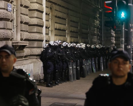 Serbian riot police with shields line a building wall at night during an election