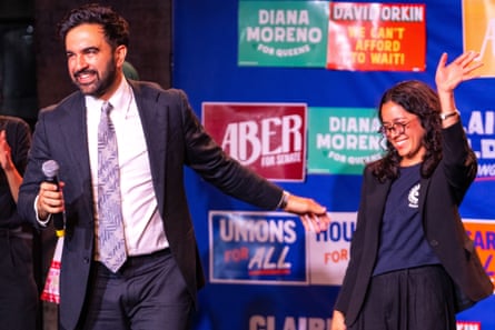 man in suit holds arm out towards woman smiling and waving to crowd