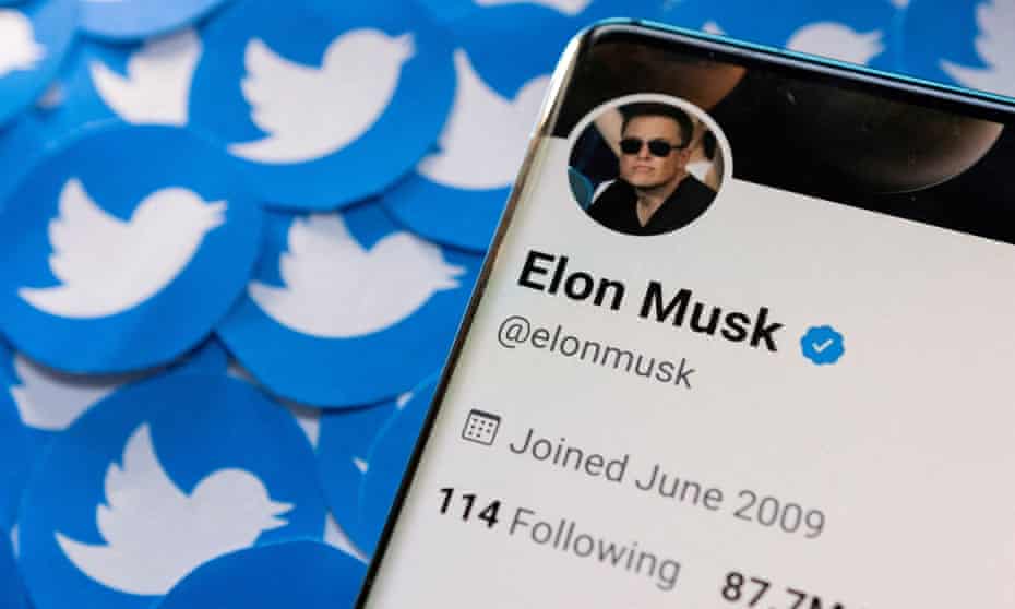 Elon Musk's Twitter profile is seen on a smartphone placed on printed Twitter logos