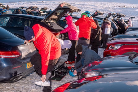 Lines of cars parked in snow with boots open and people changing their shoes