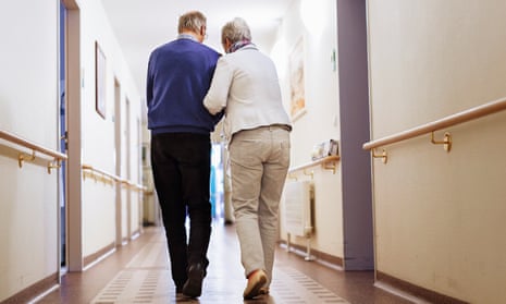an elderly man and woman walk down a corridor