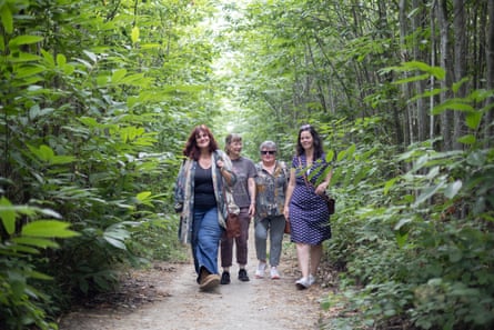 The four women walk along a path in the woods surrounded by tall, green trees