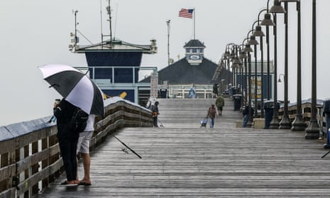 People stand on a pier under a large umbrella to avoid the wind and rain.