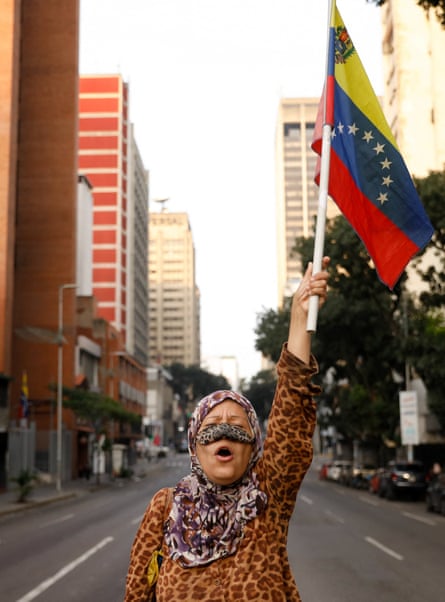 Bir kadın, ıssız bir şehir sokağında Venezuela bayrağını havaya kaldırıyor.