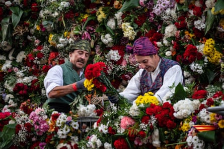 Two men in traditional costumes surrounded by flowers as they arrange more